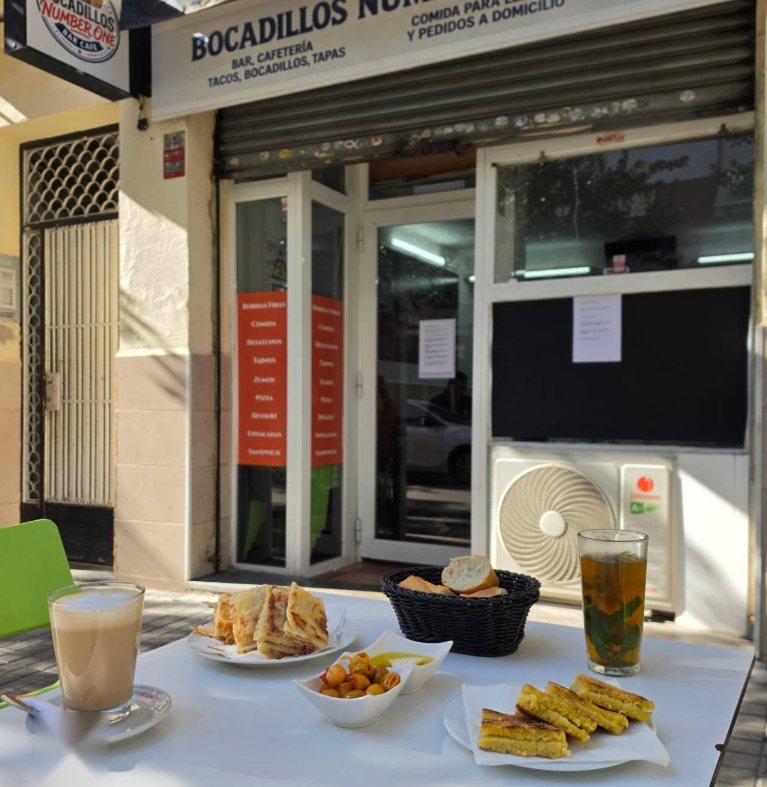 Mesa en la terraza con msemen, harcha, pan, aceitunas, té con menta y café con leche, delante del local Bocadillos Number One